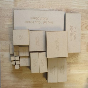 May include: A collection of laser-cut cardboard pieces, including rectangular and square shapes, with various sizes and text labels. The largest piece is labeled "Hvy Inf / Cav Horde 250x100mm". Other pieces are labeled "Inf Horde 200x80mm" and "Titan 75x75".