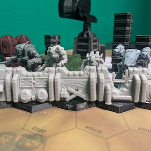 May include: A close-up of a miniature wargaming scene featuring grey and brown plastic figures, a grey wall, and a brown hexagonal game board with text. The figures are positioned on the wall and the board.