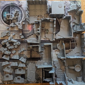 May include: A set of grey plastic building pieces for a tabletop game. The pieces are designed to look like a ruined city, with walls, floors, and other details. The pieces are arranged on a grey and white gridded surface.