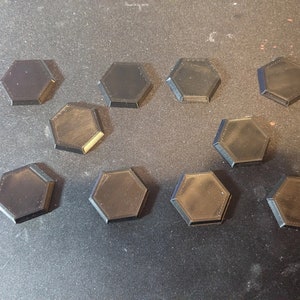 May include: Twelve black hexagonal plastic bases for miniature figures. The bases are all the same size and shape.