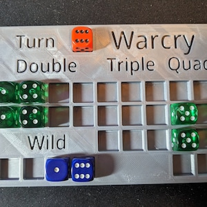 May include: A gray plastic game board with the words "Warcry", "Triple", and "Quad" printed on it. The board has a grid of squares and is used to track dice rolls. There are several dice on the board, including red, green, and blue dice.