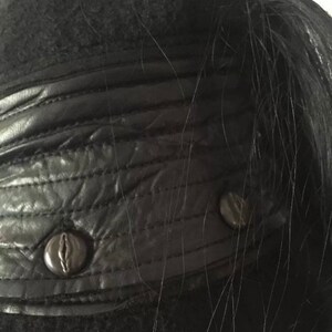 May include: Close-up of a black leather jacket with a black fur collar and two black buttons.