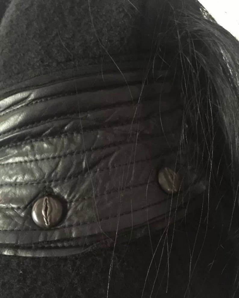 May include: Close-up of a black leather jacket with a black fur collar and two black buttons.