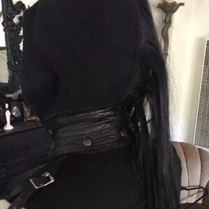 May include: A black hooded top with a black leather belt and a long black ponytail.