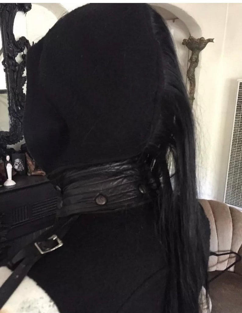 May include: A black hooded top with a black leather belt and a long black ponytail.