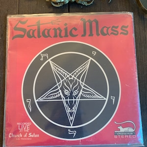 May include: A red vinyl record album with a black pentagram and the text "Satanic Mass" and "Recorded Live at the Church of Satan, San Francisco".