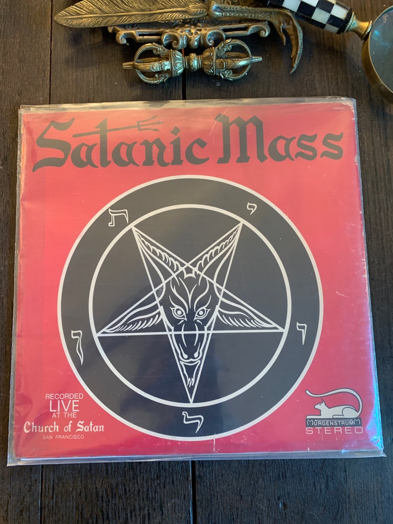 May include: A red vinyl record album with a black pentagram and the text "Satanic Mass" and "Recorded Live at the Church of Satan, San Francisco".