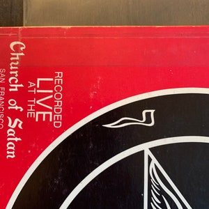 May include: A red and black vinyl record cover with the text "Recorded Live at the Church of Satan San Francisco" and a black and white pentagram with a winged symbol.