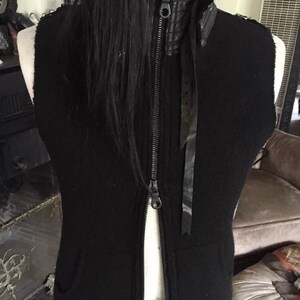 May include: Black sleeveless vest with a zip fastening and a black leather collar. The vest has a black ribbon tied at the neck.