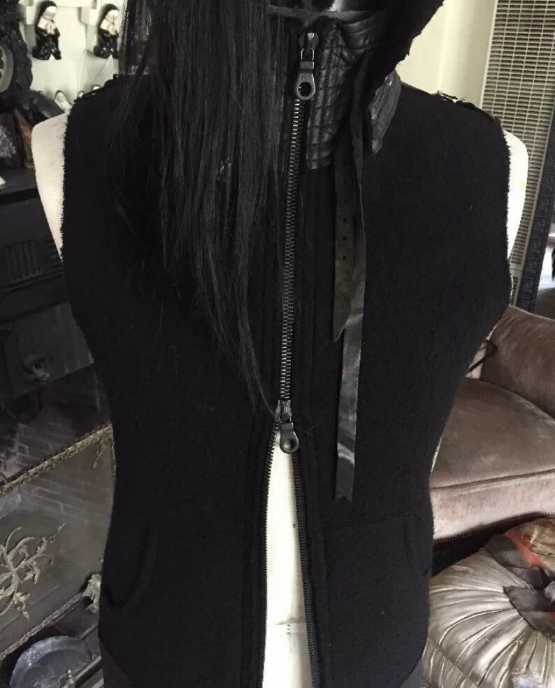 May include: Black sleeveless vest with a zip fastening and a black leather collar. The vest has a black ribbon tied at the neck.