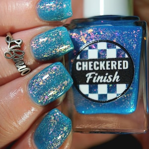 May include: A square glass bottle of bright blue nail polish with a white cap and a circular label featuring a black and white chequered pattern and the text "CHECKERED Finish". The polish contains iridescent flakes that shimmer in various colours.