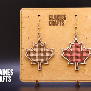 May include: A pair of wooden maple leaf earrings with a gingham pattern. The earrings are on a wooden display card with the text "Claines Crafts".