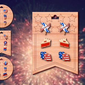 May include: A wooden display card with six pairs of patriotic-themed earrings. The earrings feature designs such as stars, pinwheels, pie slices, and the word "USA".