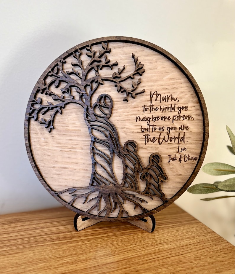 May include: A wooden circle with a carved tree design and the words "Mum, to the world you may be one person, but to us you are the world. Love Jack & Olivia" engraved on it.