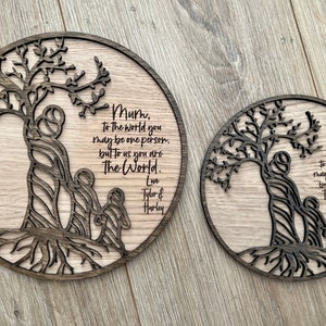 May include: Two round wooden plaques with a tree design and a message that reads "Mum, to the world you may be one person, but to us you are The World." The plaques are laser cut and have a dark wood stain.