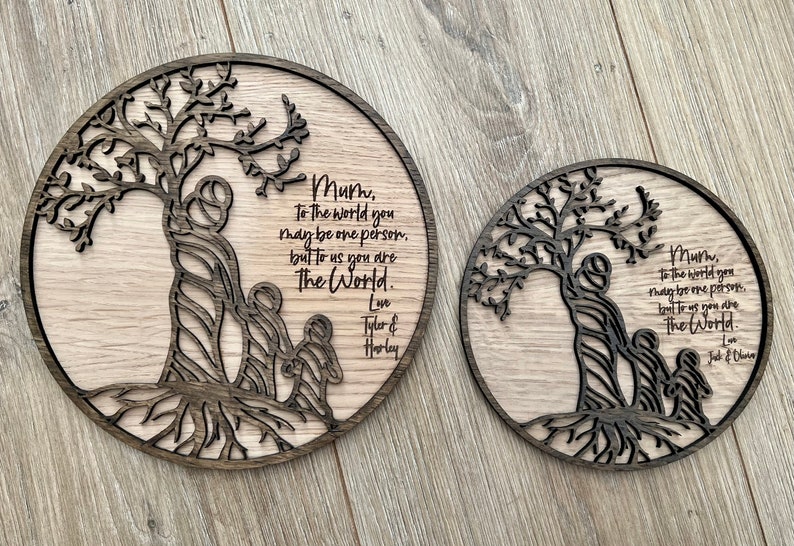 May include: Two round wooden plaques with a tree design and a message that reads "Mum, to the world you may be one person, but to us you are The World." The plaques are laser cut and have a dark wood stain.