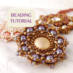 Puede incluir: Un colgante de cuentas con forma de flor que presenta un cabujón central de oro mate rodeado de perlas moradas iridiscentes y cuentas de semillas de bronce metálico. Un cuadro de texto con las palabras BEADING TUTORIAL se superpone.