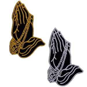 May include: Two embroidered iron-on patches featuring praying hands with a chain and cross. One patch is gold and the other is white.