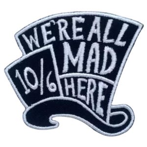 May include: Black and white embroidered patch with a hat and the text "We're all mad here 10/6".