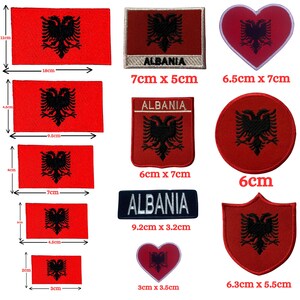 May include: A selection of Albanian flag patches in different shapes and sizes. The patches display a red background with a black double-headed eagle emblem. Sizes vary from 2 cm to 11 cm in length. Some patches include the word "ALBANIA".