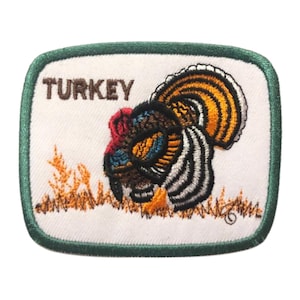Può includere: Toppa ricamata con sfondo bianco e bordo verde. La toppa presenta un'immagine colorata di un tacchino con la parola "TURKEY" in testo marrone sopra il tacchino.