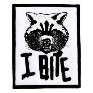 May include: Black and white embroidered patch featuring a raccoon face and the text "I Bite".