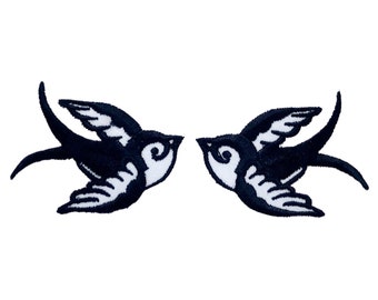 May include: Two black embroidered swallow birds facing each other with white accents.