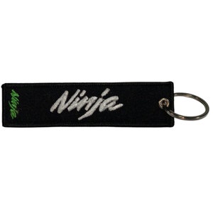 May include: Black rectangular keychain with the word "Ninja" embroidered in white script. The word "Ninja" is also embroidered in green on the left side. A silver key ring is attached to the right end.