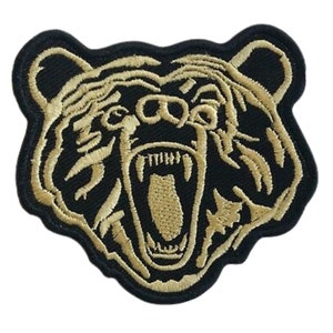 May include: A gold embroidered patch of a bear's head with an open mouth and sharp teeth. The bear's head is outlined in black.