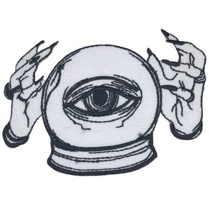 Peut inclure: Un patch brodé noir et blanc représentant un globe de cristal avec un œil à l'intérieur, tenu par deux mains à griffes.