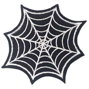 Può includere: Toppa in tessuto nero con un disegno di ragnatela ricamato in bianco.