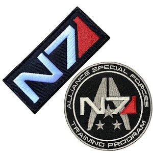 以下が含まれることがあります： Mass EffectビデオゲームシリーズのN7ロゴが刺繍された2つのパッチ。最初のパッチは、白と赤のN7ロゴがついたシンプルな黒い長方形。2番目のパッチは、白と赤のN7ロゴがついた円形のパッチで、周囲に「Alliance Special Forces Training Program」の文字が書かれています。