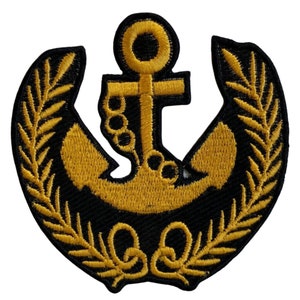 Puede incluir: Un ancla bordada en oro con una cadena y una corona de hojas alrededor. El ancla y la corona están sobre un fondo negro.