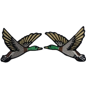 Könnte beinhalten: Zwei gestickte Aufnäher von fliegenden Enten. Die Enten sind braun, grau und grün. Die Aufnäher sind perfekt, um Ihren Kleidungsstücken oder Accessoires einen Hauch von Natur zu verleihen.