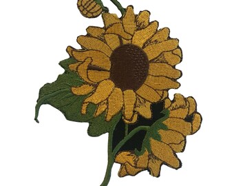 Pode incluir: Patch de girassol bordado com uma flor amarela grande e aberta com centro castanho, duas flores menores, folhas verdes e um botão. O patch é projetado com costuras detalhadas e um fundo branco.