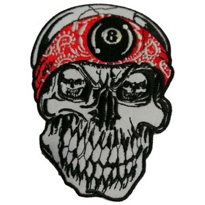 Peut inclure: Crâne blanc avec un bandana rouge et une boule noire de 8 dessus. Le crâne a une expression menaçante avec des dents acérées.
