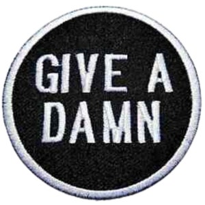 May include: Black and white embroidered patch with a white circle border. The text "GIVE A DAMN" is embroidered in white on a black background.