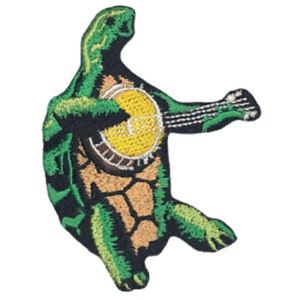 以下が含まれることがあります： 黄色の顔と白い縁取りのあるバンジョーを弾いている緑色のカメ。カメは足を伸ばして立っている。