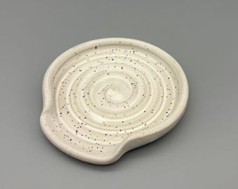 Könnte beinhalten: Weißer Keramik-Löffelhalter mit gesprenkeltem Glase und einem Spiraldesign.