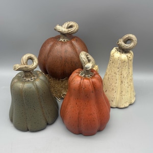 May include: Four ceramic pumpkins in shades of orange, brown, green, and cream. Each pumpkin has a twisted stem. The pumpkins vary in shape and size, with a rustic, speckled finish, perfect for fall decor.