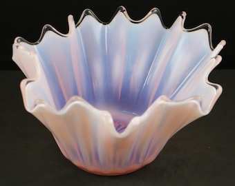 May include: A large, white, opalescent glass bowl with a ruffled rim. The bowl has a pink and blue iridescent finish.