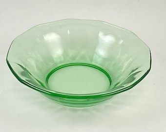 May include: A translucent light green glass bowl featuring a scalloped rim and a smooth, circular base. The bowl has a shallow, wide design with subtle vertical indentations along the interior walls, creating a reflective and uniform appearance.
