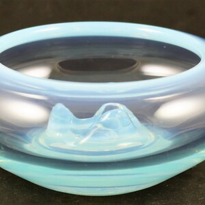 May include: A light blue glass bowl with a unique, wavy design. The bowl has a raised, opaque white center that resembles a mountain range.