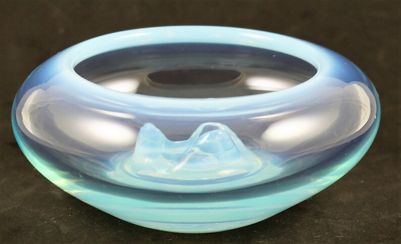 May include: A light blue glass bowl with a unique, wavy design. The bowl has a raised, opaque white center that resembles a mountain range.