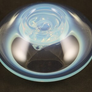 May include: A light blue glass bowl with a swirling, opaque white design in the center. The bowl has a smooth, rounded rim and a slightly flared base.