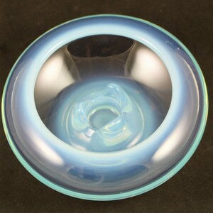 May include: A light blue glass ashtray with a wide, shallow bowl and a raised center. The ashtray has a smooth, glossy finish.