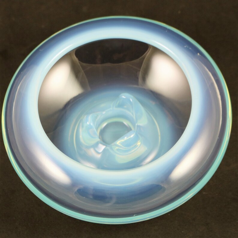 May include: A light blue glass ashtray with a wide, shallow bowl and a raised center. The ashtray has a smooth, glossy finish.