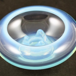 May include: A light blue glass ashtray with a raised center and a smooth, rounded rim.