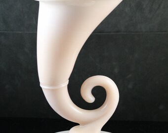 May include: A pale pink, horn-shaped vase with a wide, flared opening. The vase has a curved body that ends in a decorative swirl and sits on a round base. The vase is made of a smooth, opaque material.