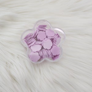 May include: A clear plastic flower-shaped container filled with small, light purple flower-shaped confetti.